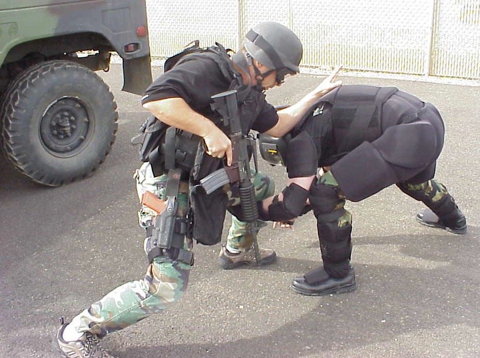 A tactical officer and a role player in High Gear during a scenario drill beside a military vehicle